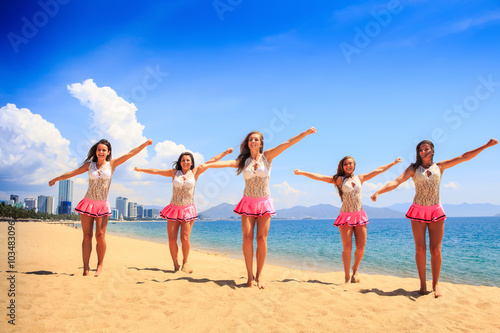 cheerleaders in dance pose bent arms on beach against sea
