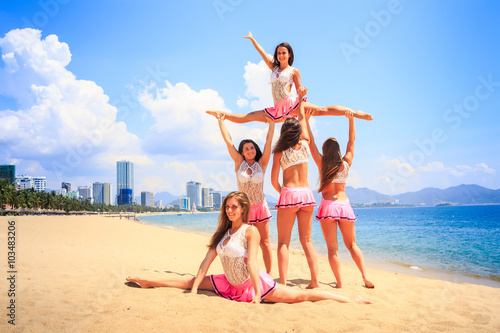 cheerleaders perform High Straddle Stunt on beach against sea