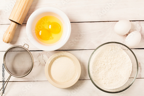 Baking in rustic kitchen recipe ingredients (eggs, flour, milk) on white  wooden table from above. 
