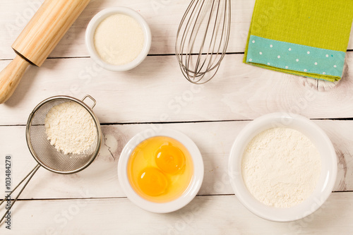 Baking in rustic kitchen recipe ingredients (eggs, flour, sugar) on white  wooden table from above. 