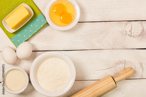 Baking in rustic kitchen recipe ingredients (eggs, flour, milk, butter, sugar) on white  wooden table from above. 