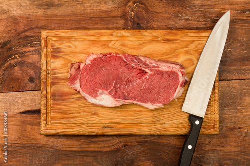 One Raw fresh meat Rib eye steak and seasoning and a knife on wooden background