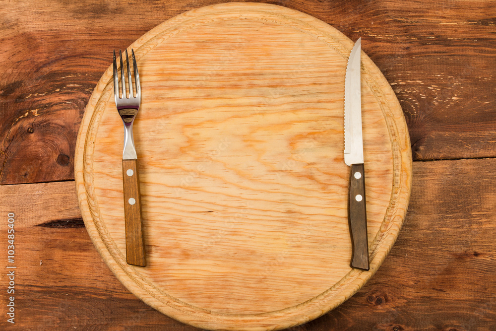 Round Chopping board, fork and knife, on wooden background
