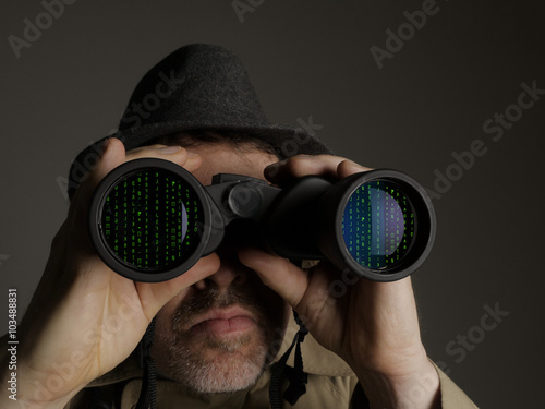 Photograph of a man in trench coat and hat looking through binoculars at computer code.