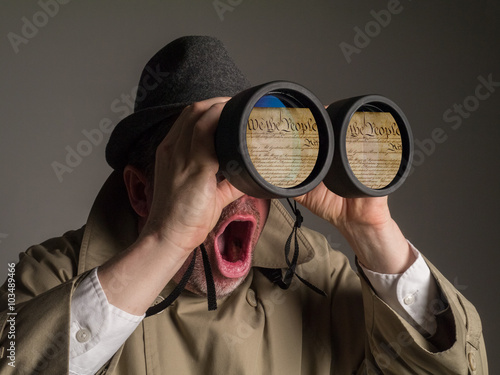 Εκτύπωση καμβά Photograph of a man in trench coat and hat looking through binoculars and shocked as he sees the Preamble to the Constitution of the United States