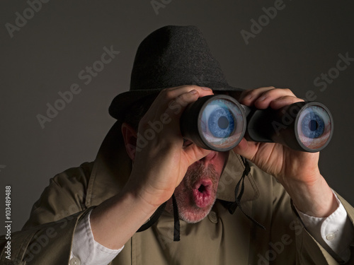 Photograph of a man in trench coat and hat looking through binoculars with huge, cartoonish eyes seen in the lenses.