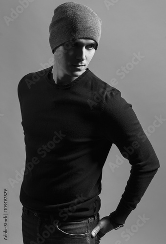 portrait of trendy guy wearing black jumpers and grey hat, arms on his pocket in jeans. the concept of a gangster guy