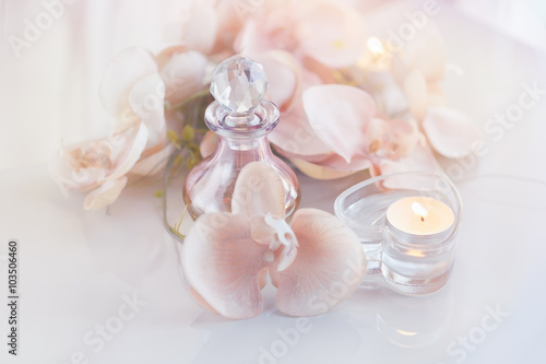Perfume or aromatic oil bottle surrounded by flowers and candles
