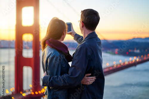 Photography couple taking photo with smart phone in front of golden gate bridge