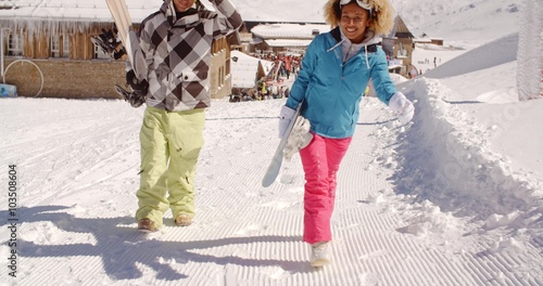 Young couple walking in heavy winter snow in a mountain ski resort carrying their snowboards