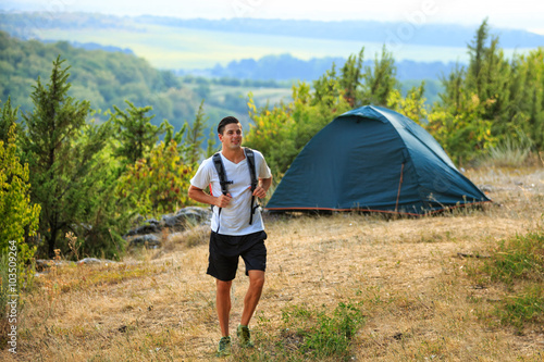 Atlethic man with backpack and tent standing on nature background