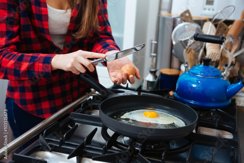 Closeup of young woman making scrambled eggs on frying pan