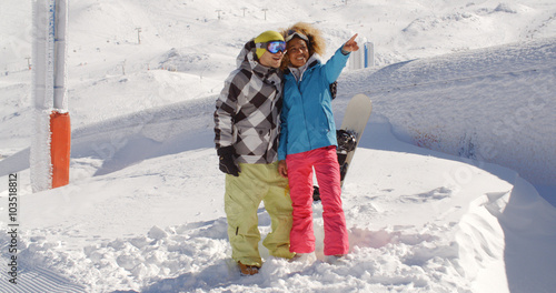 Beautiful young woman in blond curly hair pointing finger with friend at ski resort surrounded by thick white snow outside