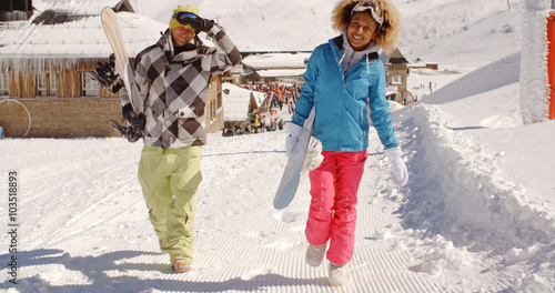 Young couple walking in heavy winter snow in a mountain ski resort carrying their snowboards