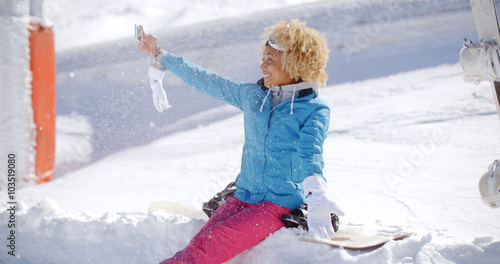 Happy young woman with a fun afro hairdo posing for a winter selfie sitting in thick winter snow at a ski resort