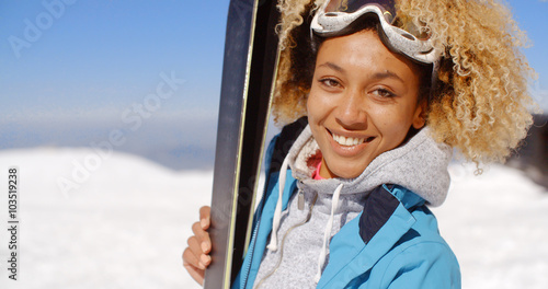 Thoughtful young woman standing holding her skis and watching something off frame to the left in a snowy winter resort landscape