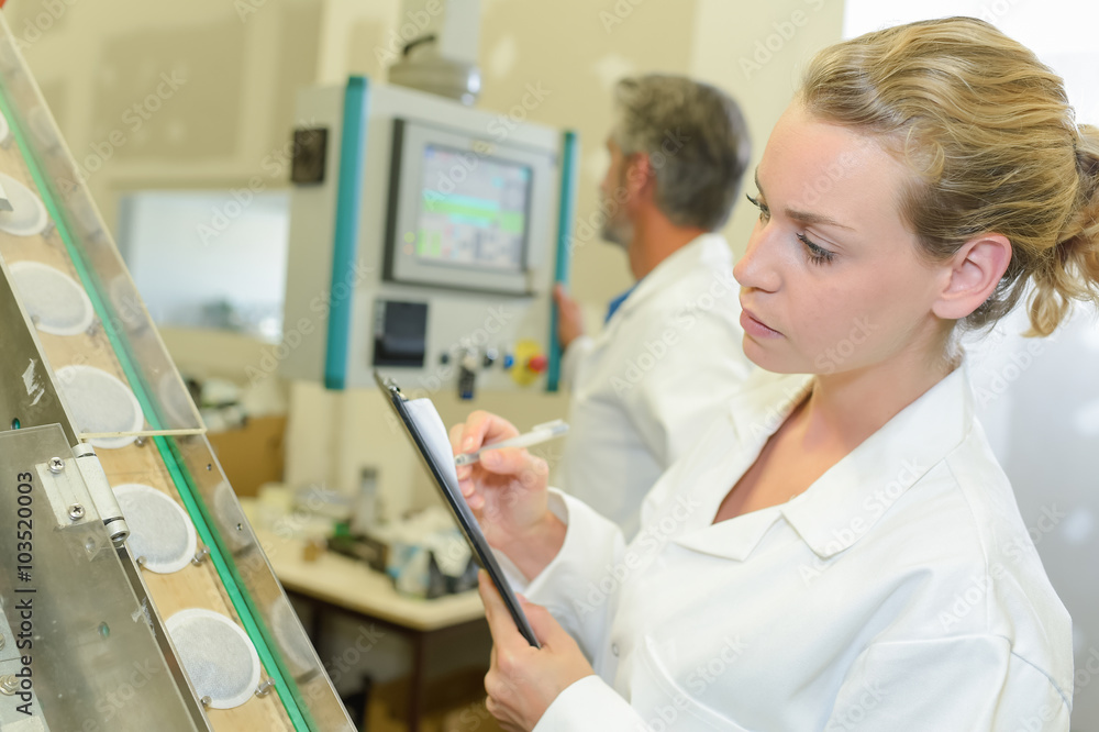 Obraz premium Lady with clipboard inspecting row of beakers