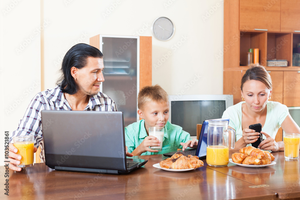 family of three using electronic devices during breakfast