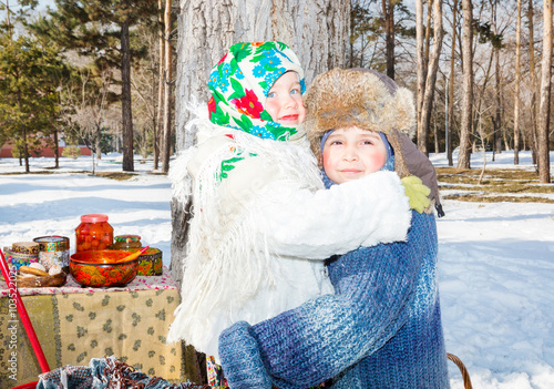 Children in Russian pavloposadskie scarf on head with floral print on snow.  Russian style on a background of samovar and with  bagels photo