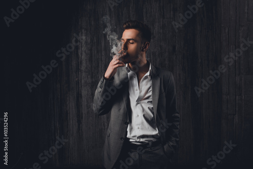 Sexy brutal man in gray suit smoking a cigar