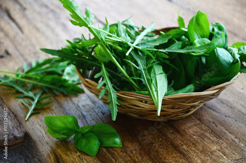 Fresh basil and arugula herbs in a wooden bowl on a wooden background