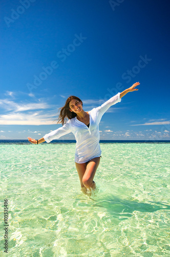Young slim woman playing in the clean sea water making airplane wings under deep blue sky. Summer vacation concept
