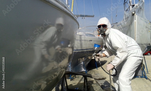 painter spray painting a boat with a paint air gun