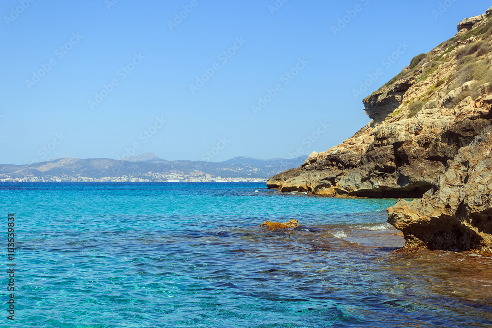 Blue and clear water at Cap Enderrocat, Llucmajor rocky coast, bay of Palma de Mallorca and Serra de Tramuntana mountains in background horizon