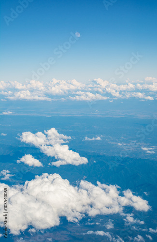 Clouds and moon in blue sky, aerial view from airplane window.