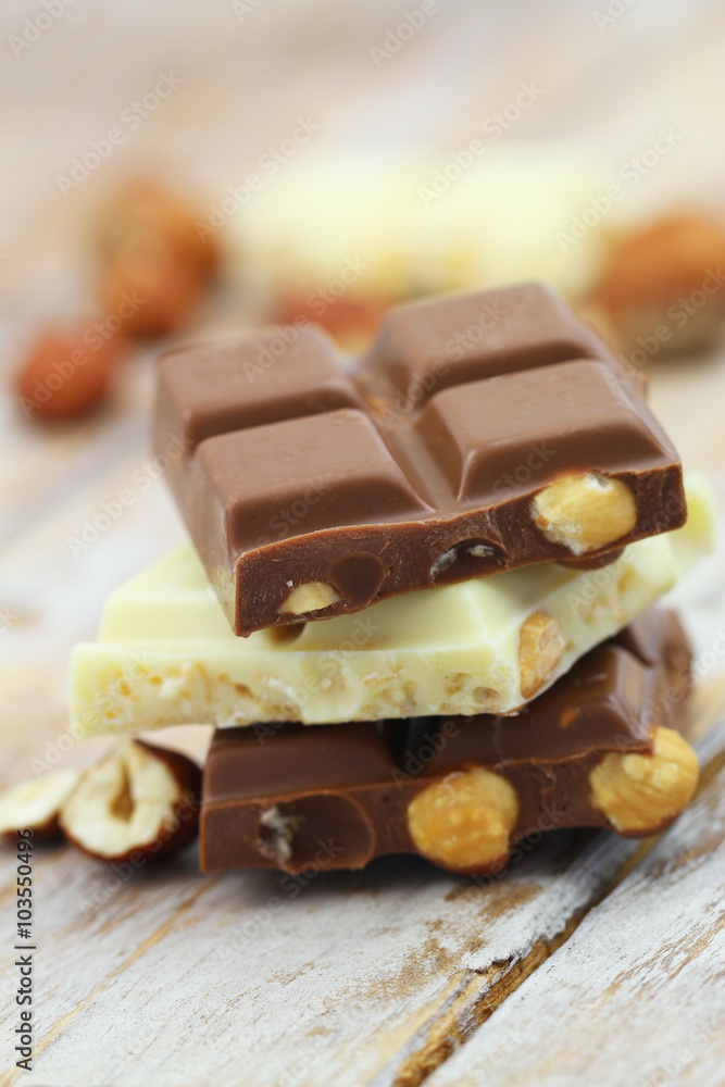 Milk and white chocolate pieces with whole hazelnuts stacked up on wooden surface
Milk and white chocolate pieces with whole hazelnuts stacked up on wooden surface