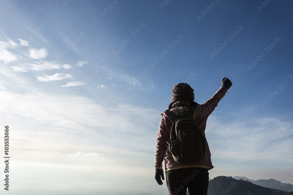 Woman with backpack standing on top of a mountain with raised ha Woman with backpack standing on top of a mountain with raised ha