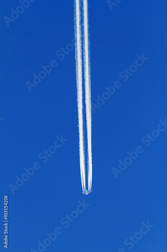 Airplane with white contrails on blue sky.