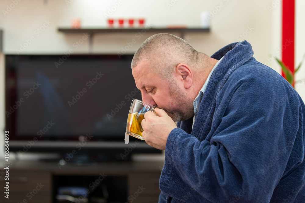 Ill man blowing his nose with paper napkin and drinking tea at home Ill man blowing his nose with paper napkin and drinking tea at home