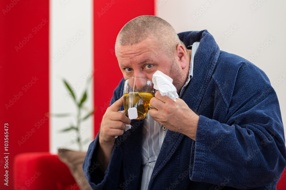 Ill man blowing his nose with paper napkin and drinking tea at home Ill man blowing his nose with paper napkin and drinking tea at home