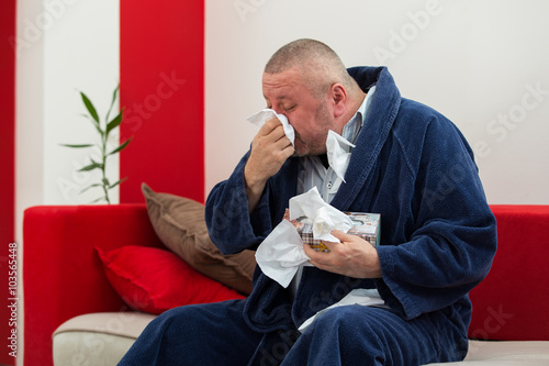 Man having a cold holding tissue with box full of tissues