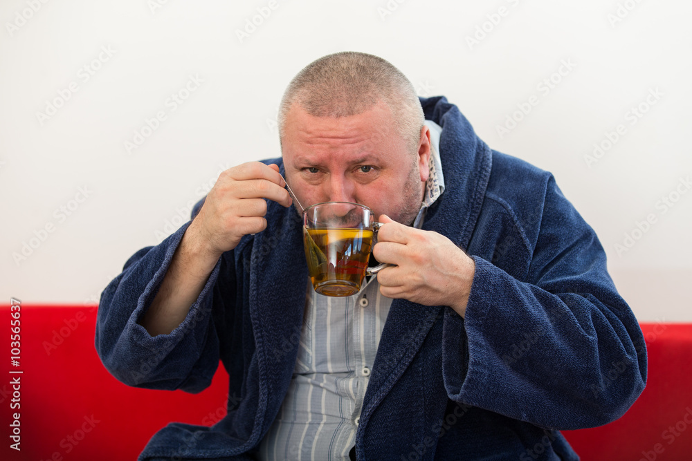 Ill man blowing his nose with paper napkin and drinking tea at home Ill man blowing his nose with paper napkin and drinking tea at home