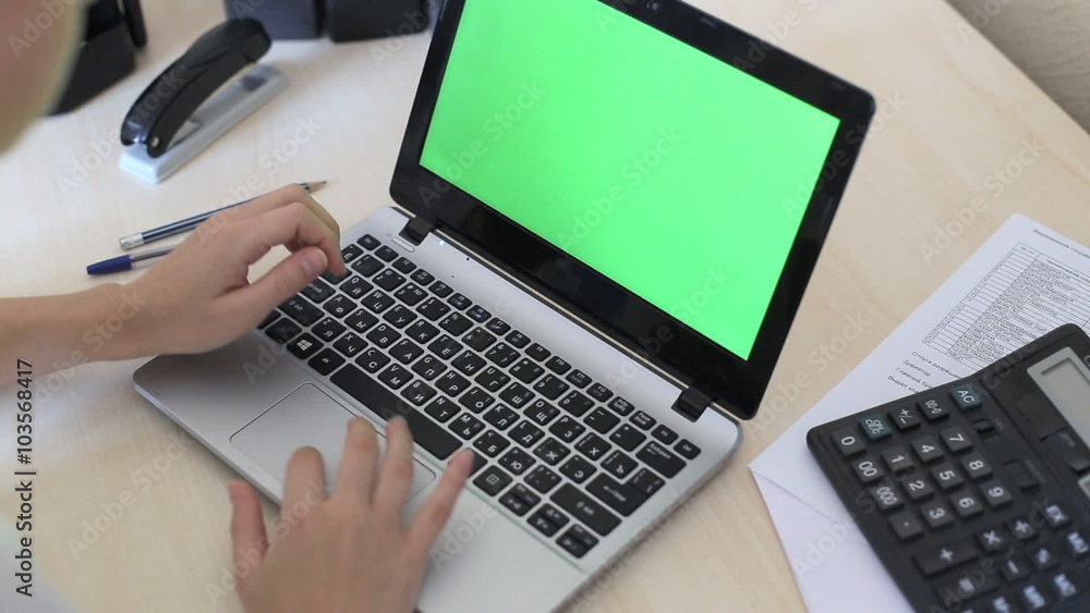 Over the shoulder shot of a woman typing on a laptop with a key-green screen.