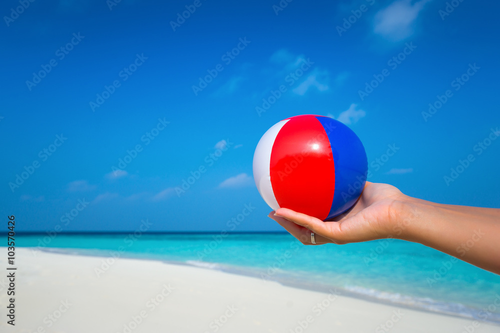 Obraz premium female hand holding a ball at a beautiful beach with a turquoise