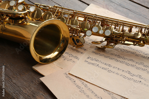 Quadro su tela Beautiful golden saxophone with musical notes on wooden background, close up