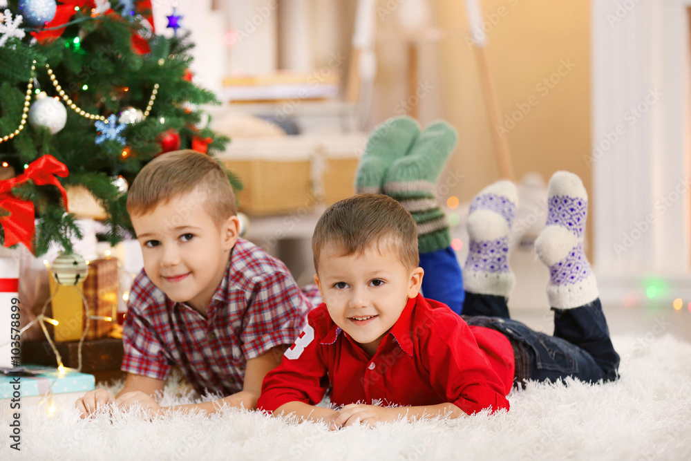 Two cute small brothers lie on carpet on Christmas tree background Two cute small brothers lie on carpet on Christmas tree background