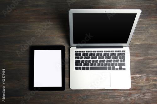 An open silver laptop and modern tablet on the wooden background