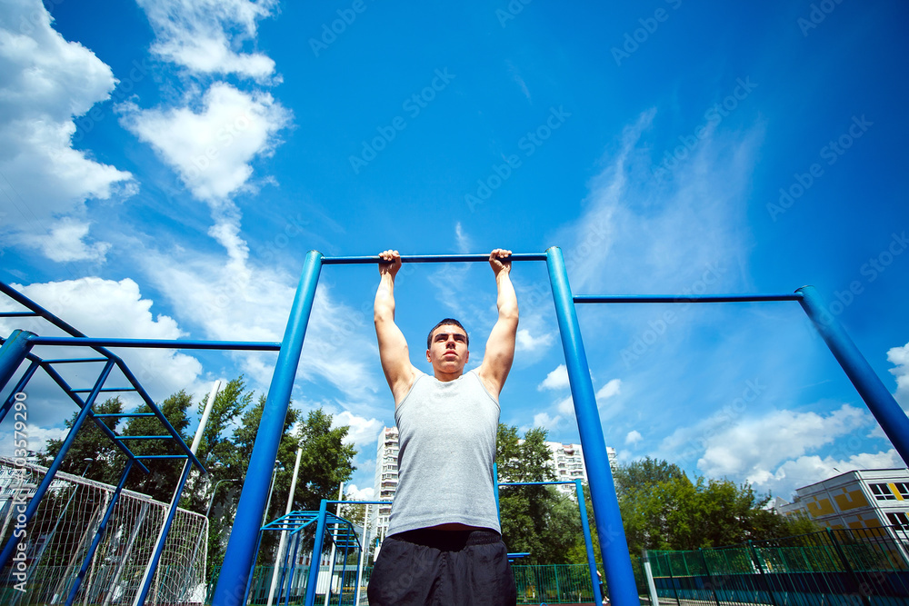 Fototapeta premium Muscular man doing pull-ups on horizontal bar