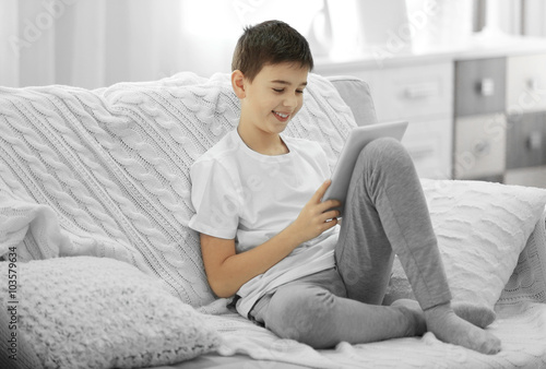 Boy using tablet on a sofa ...