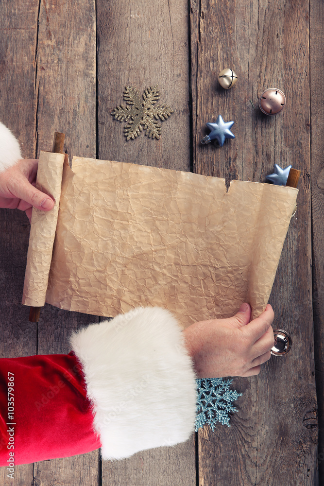 A list of Christmas wishes in Santa Claus hands on wooden background A list of Christmas wishes in Santa Claus hands on wooden background