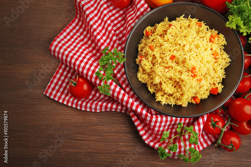 Stewed rice with a carrot on a black plate over wooden background