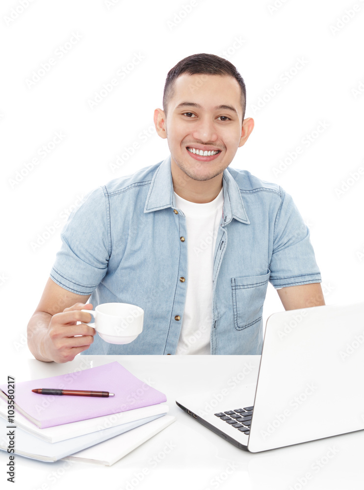 handsome young man studying on laptop while holding a cup of tea handsome young man studying on laptop while holding a cup of tea