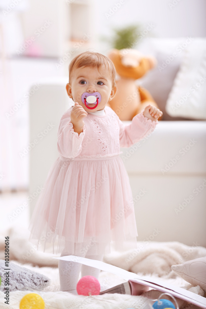 Sweet baby girl with a soother standing on floor Sweet baby girl with a soother standing on floor