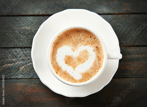 Cup of hot cappuccino with cream heart on a black wooden table