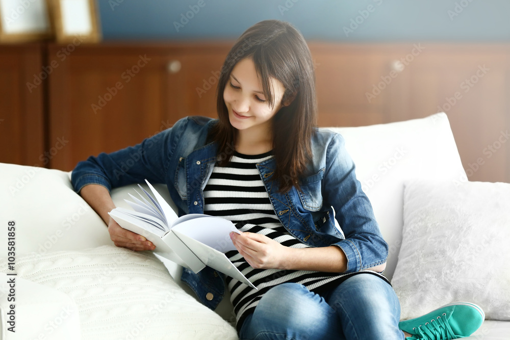 Beautiful girl reading book on sofa, indoor Beautiful girl reading book on sofa, indoor