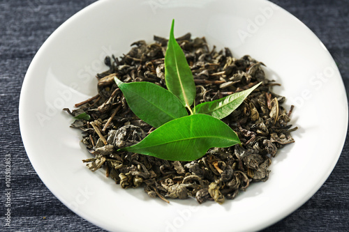 Granulated tea with green leaves in white saucer closeup